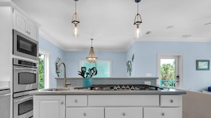 A kitchen with white cabinetry, stainless steel appliances, a central island with drawers, pendant lights, and a view of greenery outside. - 0.2 Mi to Beach, Tiki Bar, Huge Pool, Close to Silver Sands Shopping (Miramar Beach)