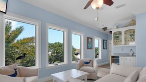 A spacious living room with a large window, a ceiling fan, and a kitchen area with cabinets. - 0.2 Mi to Beach, Tiki Bar, Huge Pool, Close to Silver Sands Shopping (Miramar Beach)