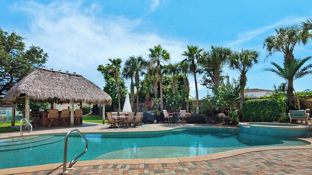 A swimming pool with lounge chairs and a thatched-roof structure. - 0.2 Mi to Beach, Tiki Bar, Huge Pool, Close to Silver Sands Shopping (Miramar Beach)