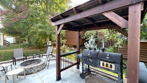 Un espace extérieur abrité, aménagé pour les barbecues, avec un foyer en pierre, des bancs en bois et un gril.