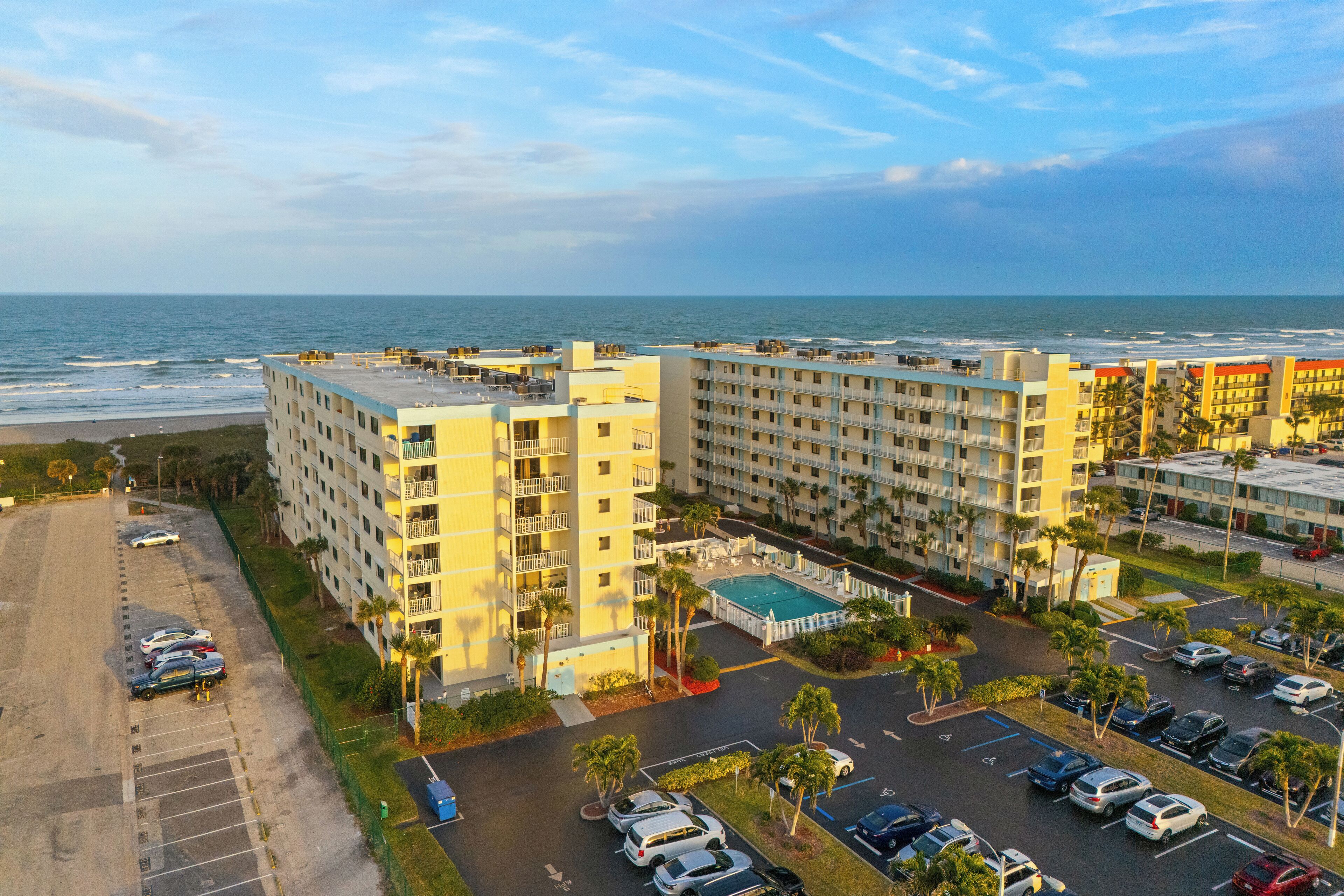 A hotel with multiple floors, a swimming pool, and a parking lot with cars.