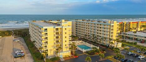 A hotel with multiple floors, a swimming pool, and a parking lot with cars.