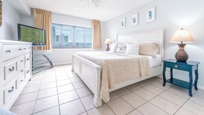 Een slaapkamer met een bed, een televisie, een dressoir, een nachtkastje en een raam met gordijnen.