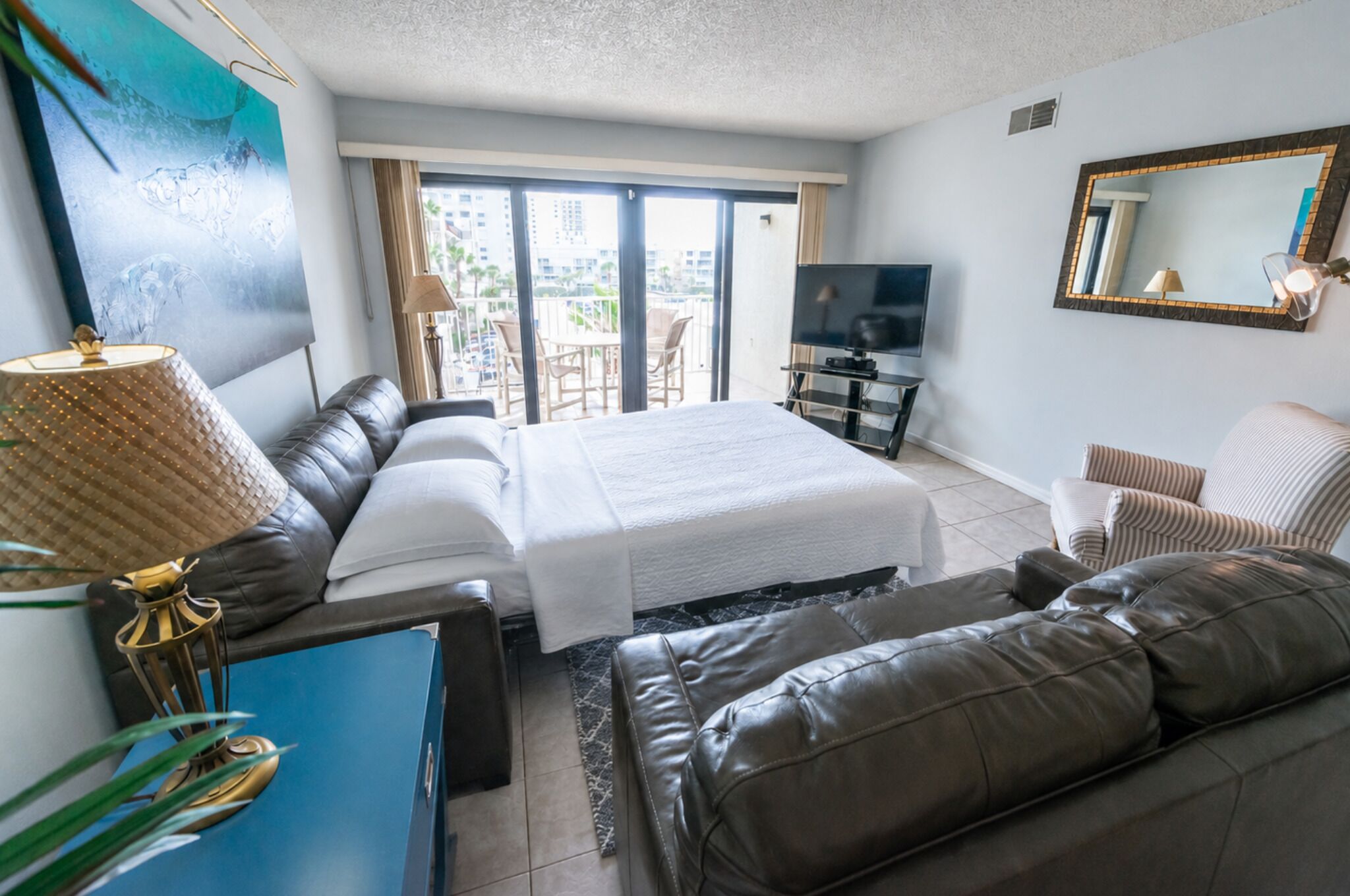 Habitación de hotel con cama, sofá, televisor y balcón con vistas a edificios.