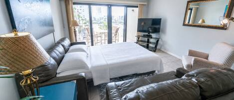 Habitación de hotel con cama, sofá, televisor y balcón con vistas a edificios.