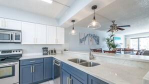 Een moderne keuken met witte en blauwe kastjes, roestvrijstalen apparatuur en hangende lampen.