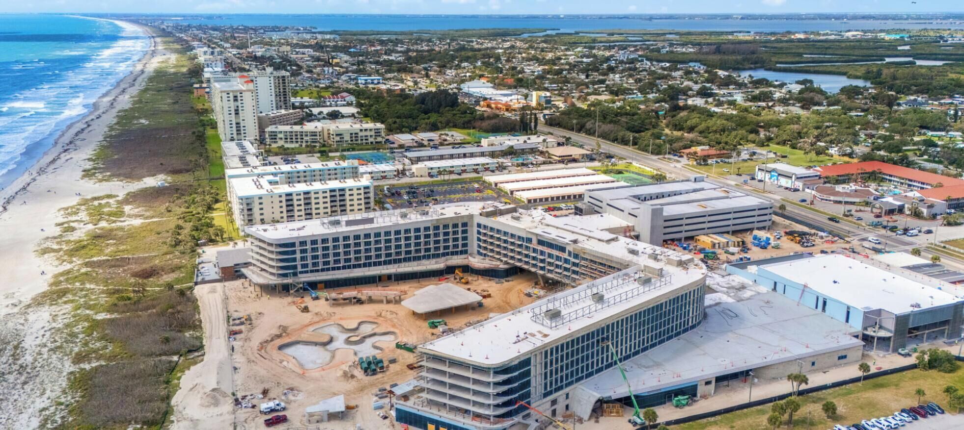 A coastal urban area with a beachfront, multi-story buildings, and a large parking lot.