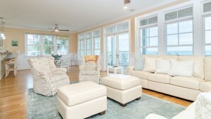 A spacious living room with a large window, a ceiling fan, and a beige sofa.