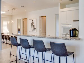 A modern kitchen with a bar area, stainless steel appliances, and a framed picture on the wall.