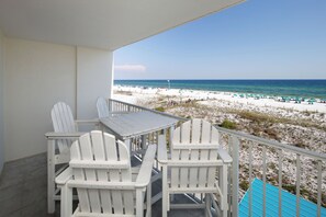 A balcony with white Adirondack chairs and a table, overlooking a beach with umbrellas and people. - GD 307: Seaglass Cove - Step Out, Chill Out... Beachfront Living at Its Best! (Fort Walton Beach)