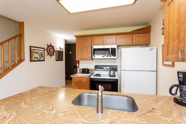 A kitchen with granite countertops, wooden cabinets, a stainless steel sink, a microwave, a stove, and a refrigerator.
