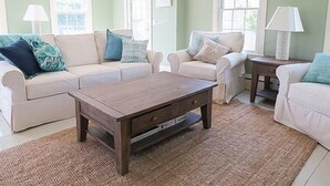 A living room with two white sofas, a wooden coffee table, and a rug. - Charming house located in the heart of downtown Chatham! (Chatham)