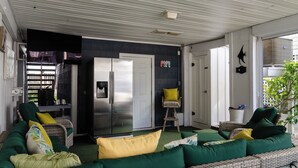 A covered outdoor living area with a sofa, chairs, a refrigerator, and a small table. - 3 Bedroom Townhome Steps from Johnnie Mercer’s! (Wrightsville Beach)