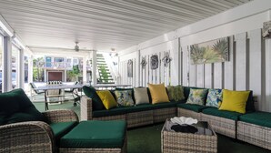 A covered outdoor seating area with wicker furniture, a table, and a staircase leading to an upper level. - 3 Bedroom Townhome Steps from Johnnie Mercer’s! (Wrightsville Beach)