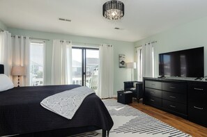 Quarto com cama, televisão, penteadeira e vista para varanda.