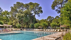 A swimming pool with lounge chairs and umbrellas, surrounded by trees. - Walk to Beach: Resort-Style Hilton Head Condo! (Hilton Head Island)