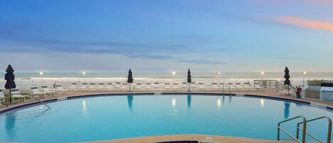 A swimming pool with a view of the beach at sunset.