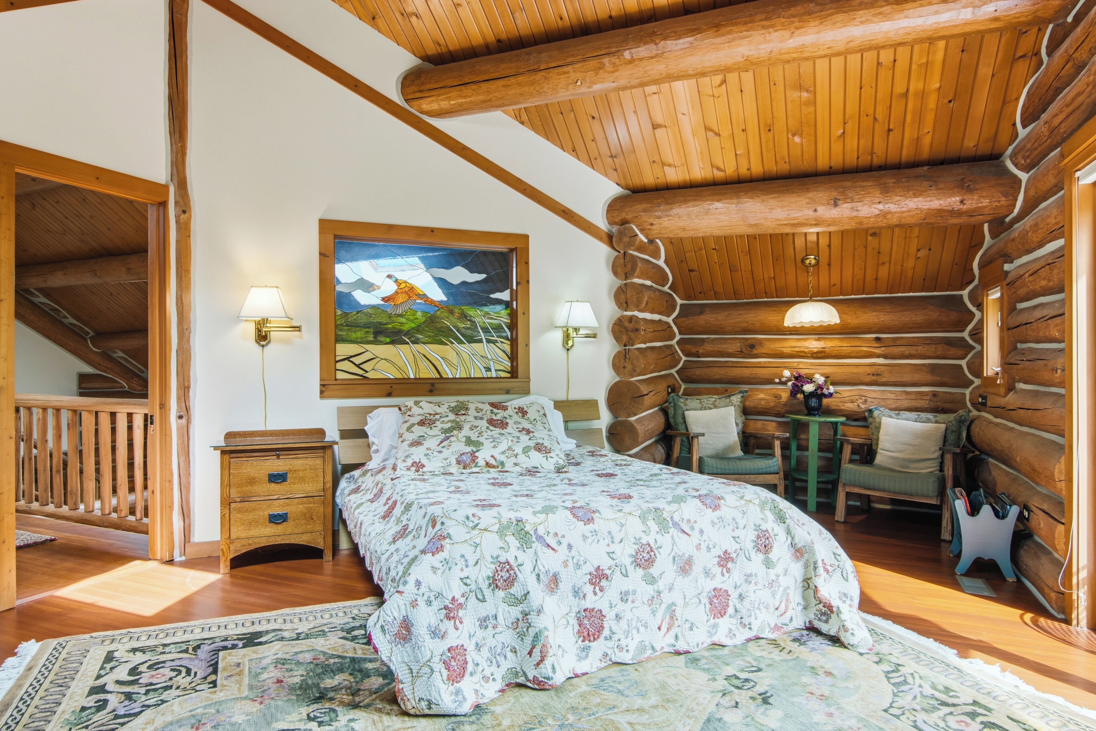 Une chambre à coucher située dans une cabane en rondins, avec un lit, deux tables de chevet, un tableau et un escalier.