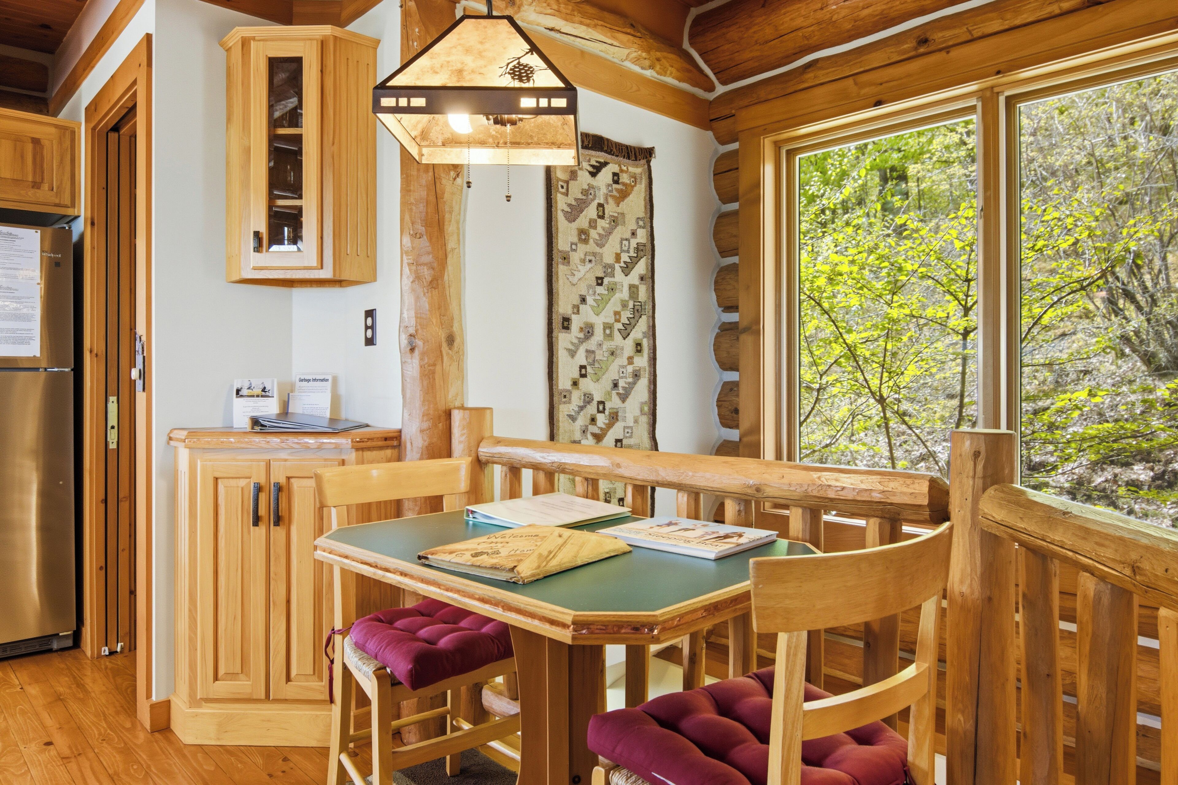 L’intérieur d’un chalet en bois comprend une table à manger, des chaises, un réfrigérateur et une fenêtre donnant sur la forêt.