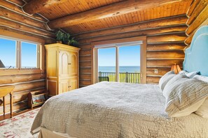 Ein Schlafzimmer in einer Blockhütte mit einem großen Bett, einem Holzschrank und einem Fenster mit Blick auf den Ozean.