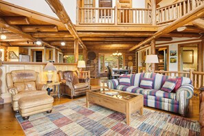 Ein Holzblockhaus-Interieur mit einer Holztreppe, Ledersesseln, einem Karo-Sofa und einem Couchtisch.