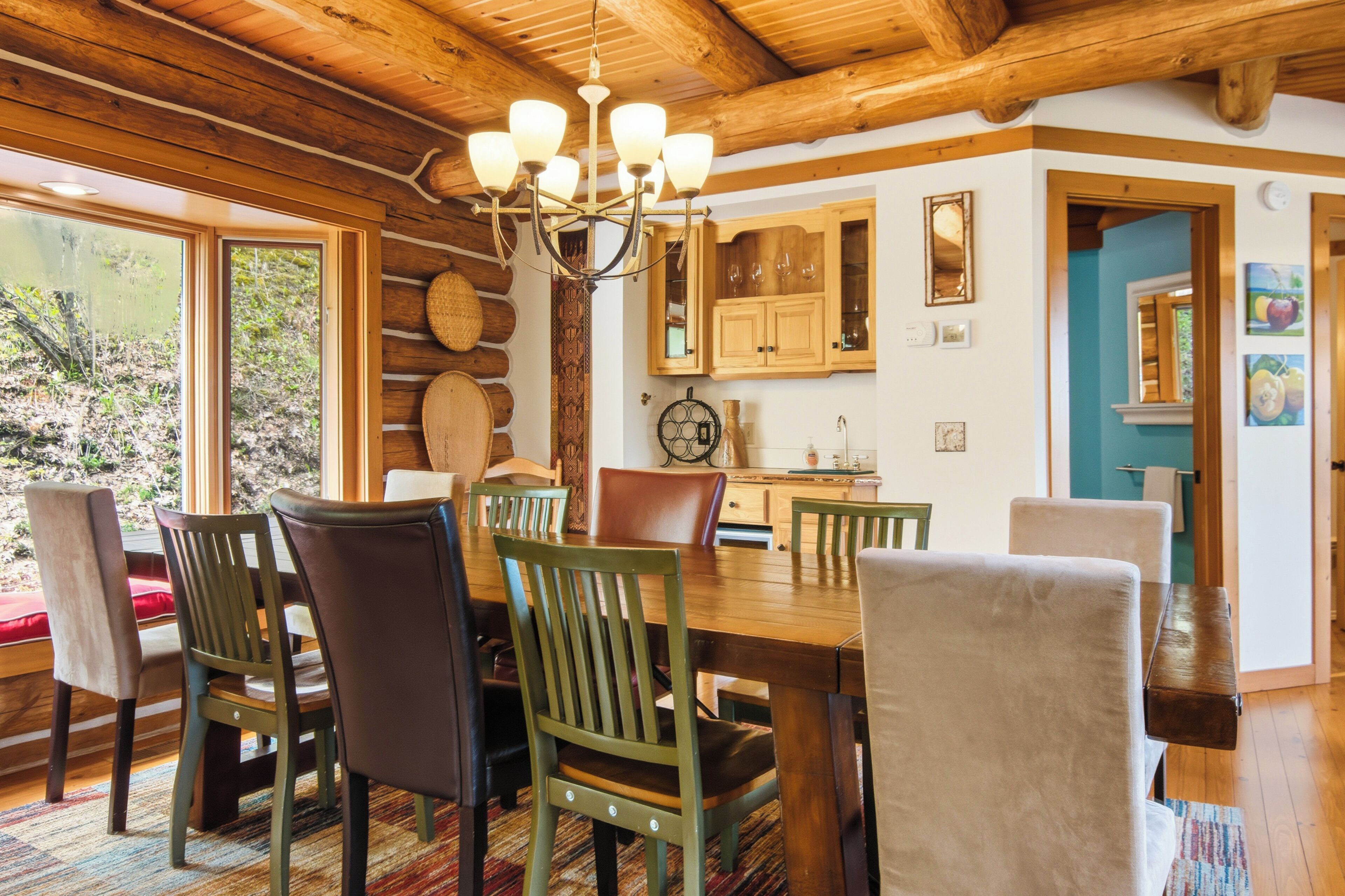 A wooden dining room with a chandelier, a large window, and a view of the outdoors.