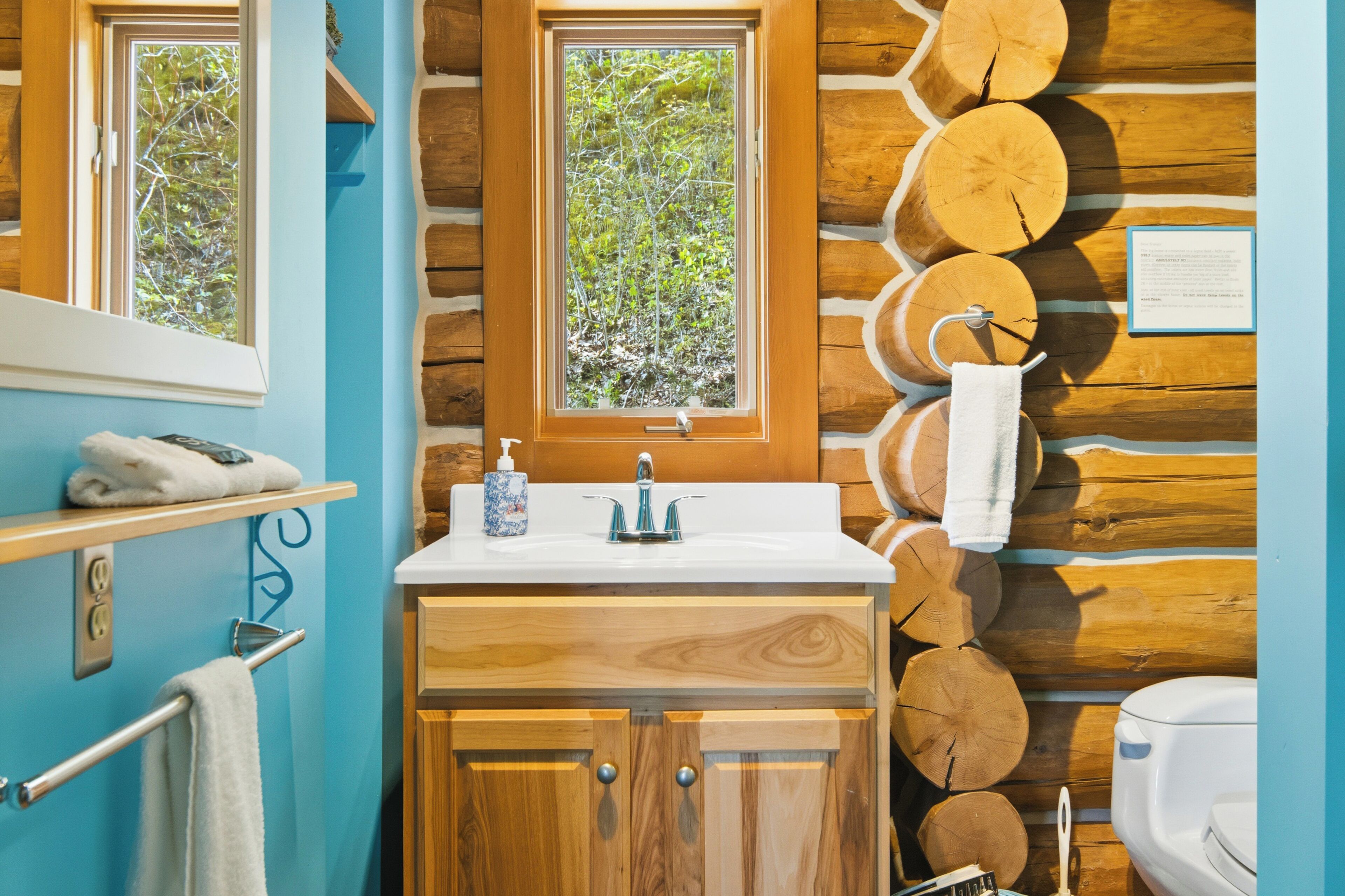 A bathroom with a wooden log wall, a window, a sink, and a toilet.