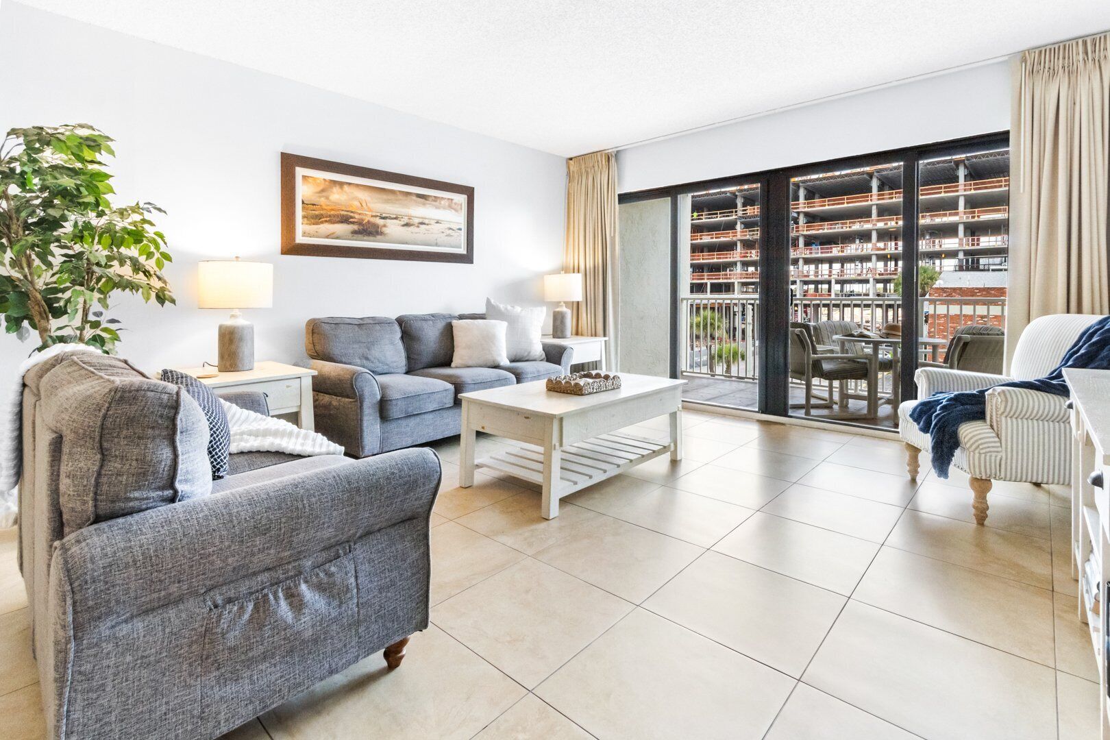 A modern living room with grey sofas, a white coffee table, and a large window with a view of a building.