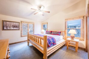 A bedroom with a wooden bed, two windows, a ceiling fan, and a framed picture on the wall.