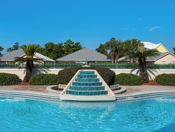 A swimming pool with a decorative fountain, surrounded by a fence and palm trees.