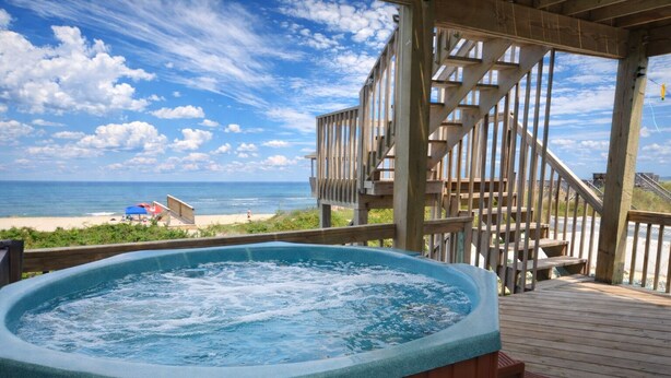Un jacuzzi en una terraza de madera con vistas a una playa y una escalera de madera.