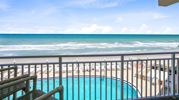 Blick auf ein Schwimmbecken mit Strand und Meer im Hintergrund.