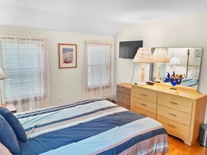 A bedroom with a bed, a dresser, a mirror, and a window with curtains. - The Cape Escape: Walk to Harding's Beach (Chatham)