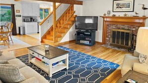 Ein Wohnzimmer mit Fernseher, Kamin und einer Treppe, die zur Küche führt.