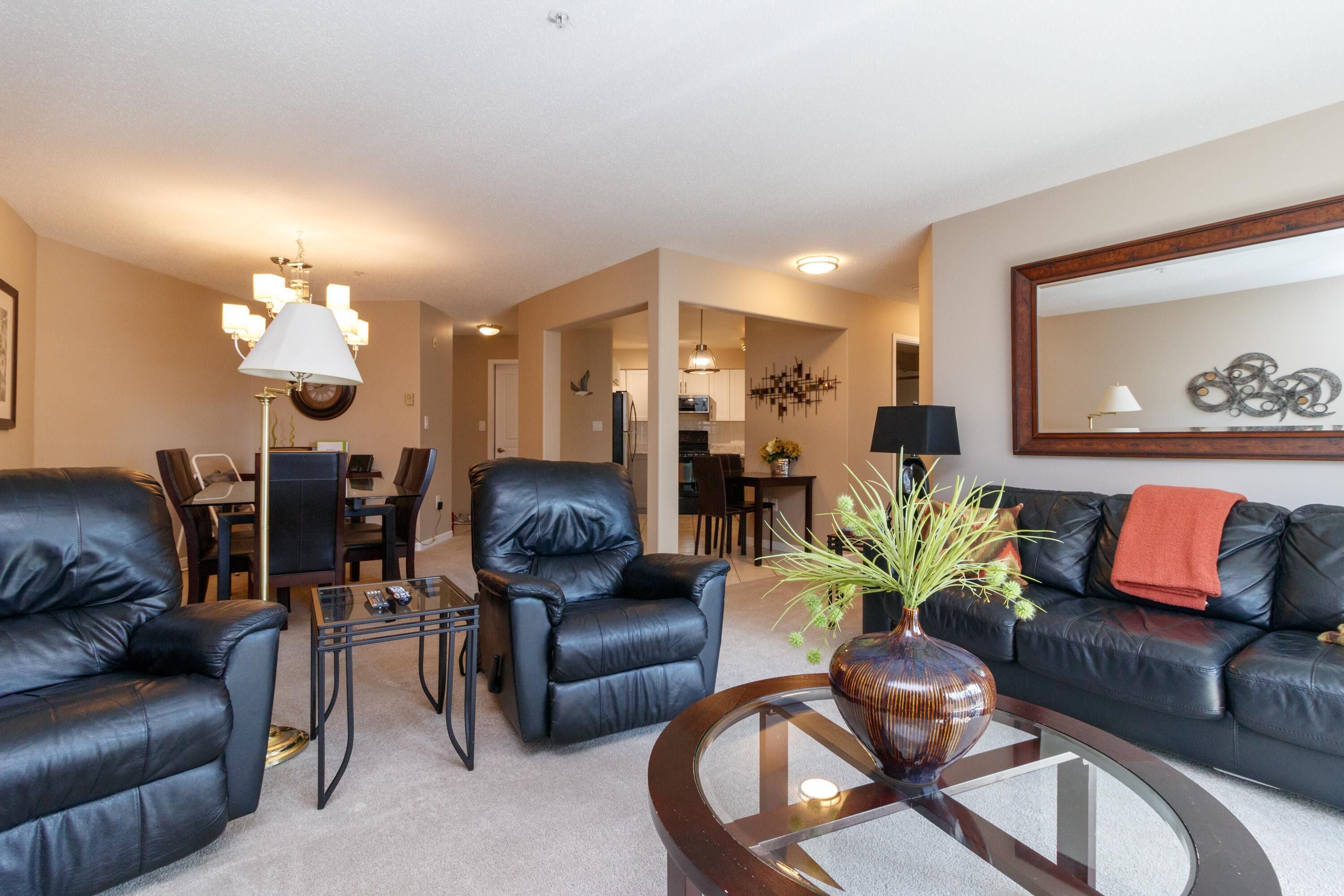 A living room with black leather sofas, a glass coffee table, and a dining area with chairs and a table.