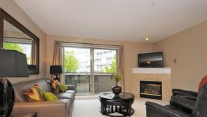 Uma sala de estar moderna com sofá, poltrona, televisão, lareira e varanda com vista para edifícios.
