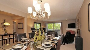 Uma sala de jantar com uma mesa comprida posta para seis pessoas, um candelabro e vista para o exterior.