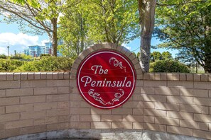 Ein rotes Schild mit dem Schriftzug "The Peninsula", umgeben von einer Backsteinmauer und Bäumen.