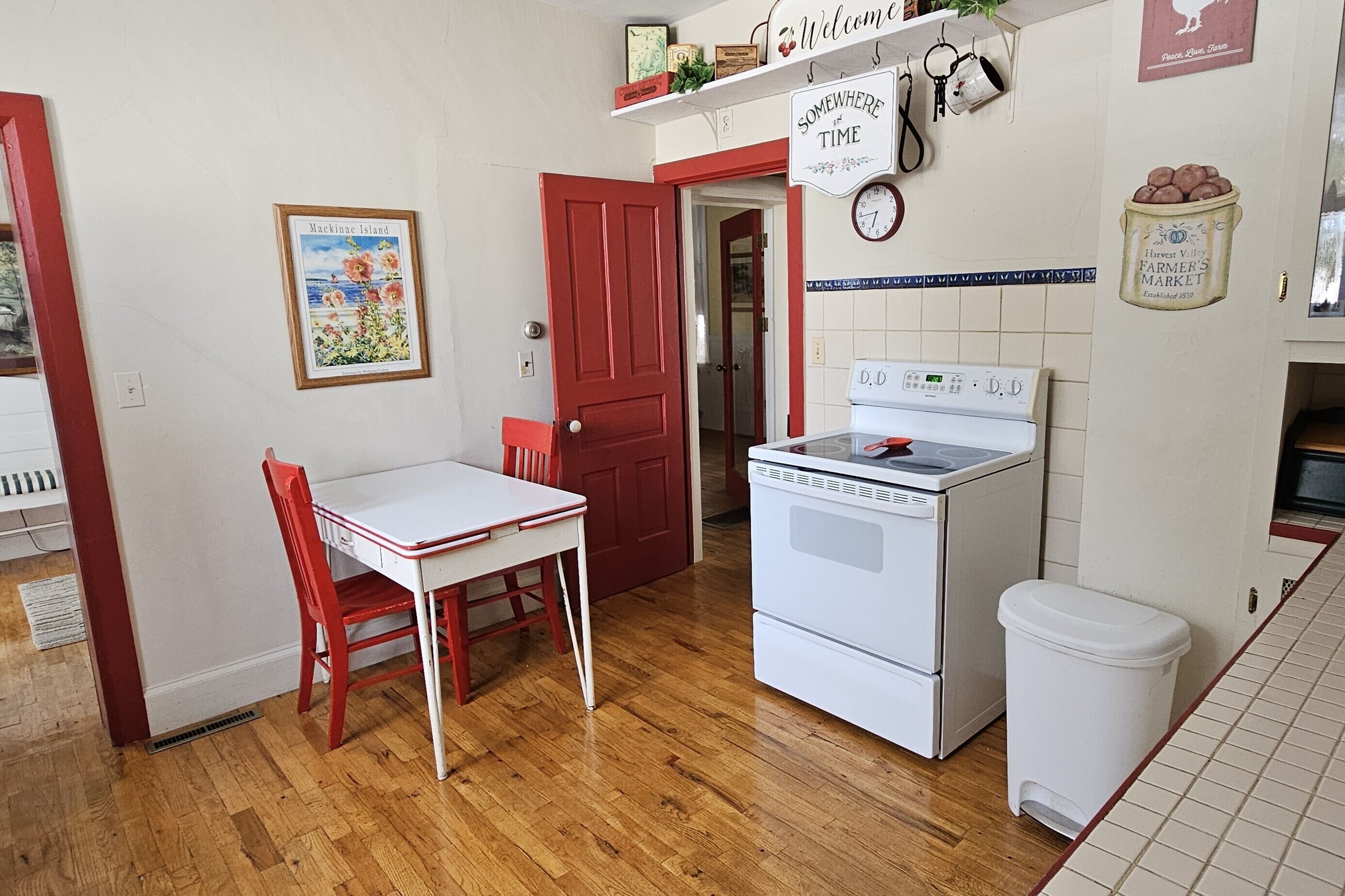 A kitchen with a white stove, a red door, and a framed picture on the wall.