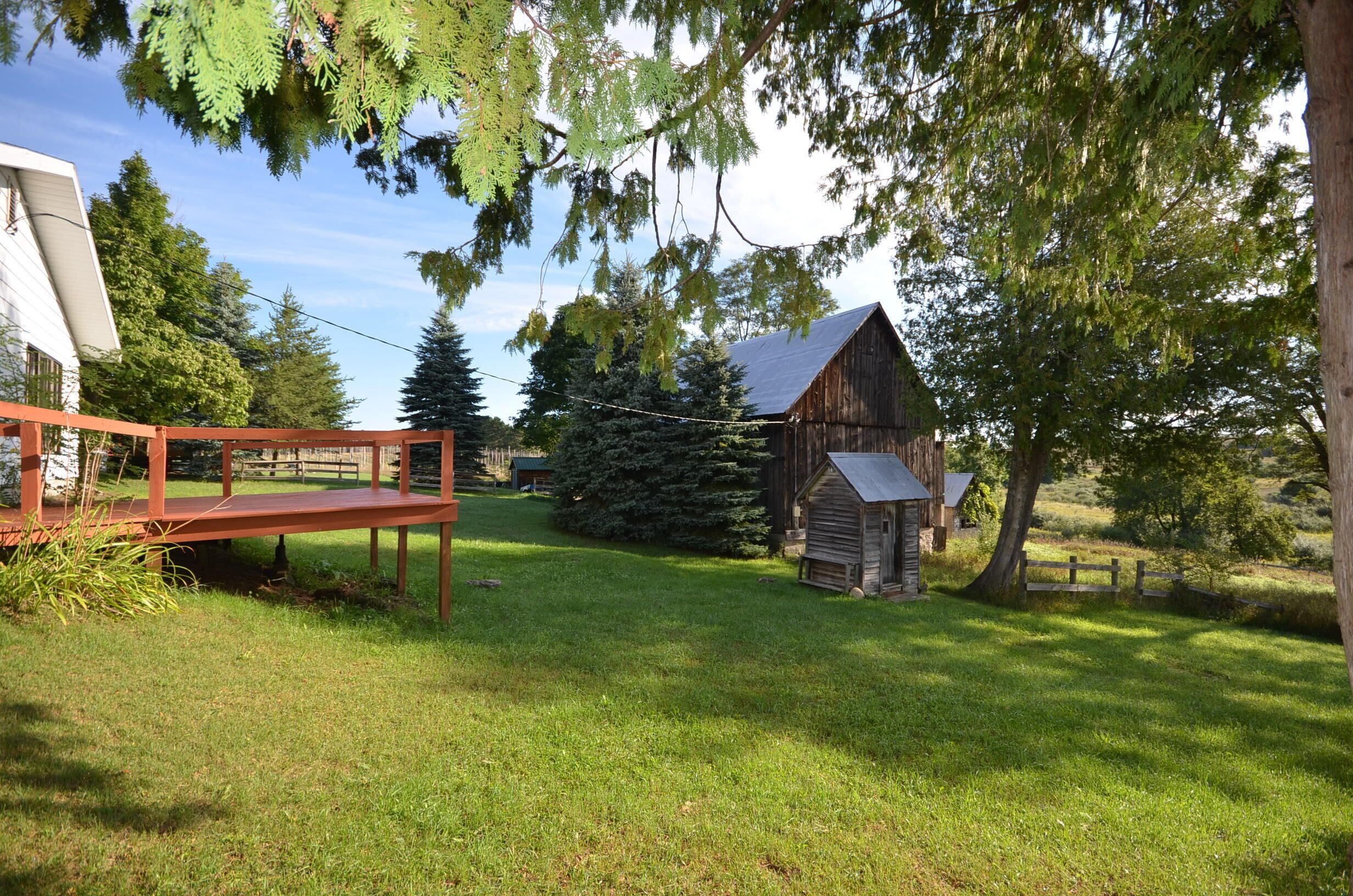 A rustic wooden barn, a wooden bench, and a small shed in a grassy area with trees.