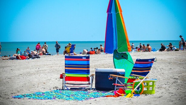 A beach with two striped beach chairs, a colorful umbrella, and a cooler on the sand. - Near Disney Parks 10 min. Themed rooms, game room, Private Pool with Screen deck (Kissimmee)