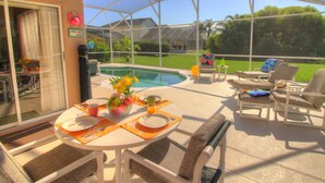 A covered patio with a pool, outdoor seating, and a table set for breakfast. - Near Disney Parks 10 min. Themed rooms, game room, Private Pool with Screen deck (Kissimmee)