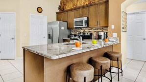 A modern kitchen with a central island, stainless steel appliances, and a rustic backsplash. - Near Disney Parks 10 min. Themed rooms, game room, Private Pool with Screen deck (Kissimmee)