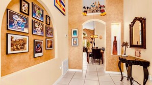 A hallway with framed Disney character pictures, a dining area with a chandelier, and a decorative mirror. - Near Disney Parks 10 min. Themed rooms, game room, Private Pool with Screen deck (Kissimmee)