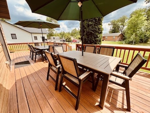 Een houten terras met tuinmeubilair, waaronder een tafel en stoelen, onder een grote parasol.