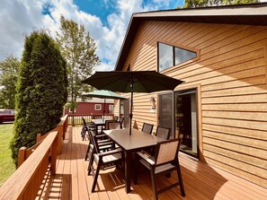 Une terrasse en bois avec une table et des chaises, un parasol vert et une maison dont la porte porte le numéro « 379 ».