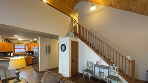Un salon spacieux avec un canapé en cuir marron, un escalier en bois et une cuisine à l’arrière-plan.