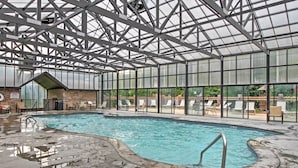Una piscina interior con techo de vidrio, sillas de descanso y pared de ladrillo.