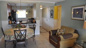 A dining area with a table and chairs, a sofa, and a kitchen in the background.