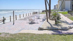 A seaside patio with outdoor seating, palm trees, and a view of the ocean.